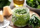 Bärlauchpesto mit Olivenöl und Parmesankäse im Glas auf einem Holztisch