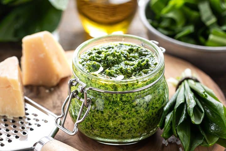 Bärlauchpesto mit Olivenöl und Parmesankäse im Glas auf einem Holztisch