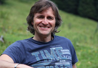 Jean Secré sitzt auf einer Bank, die auf einer grünen Bergwiese steht
