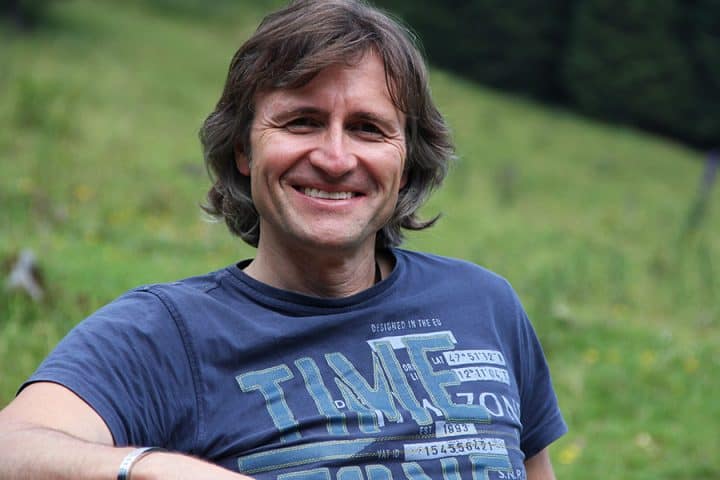 Jean Secré sitzt auf einer Bank, die auf einer grünen Bergwiese steht