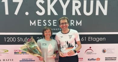 Annemarie Wilhelm und Dr. Christian Riedl stehen nach dem 17. SkyRun MesseTurm Frankfurt vor der Veranstaltungswand und präsentieren ihre Siegerpokale.