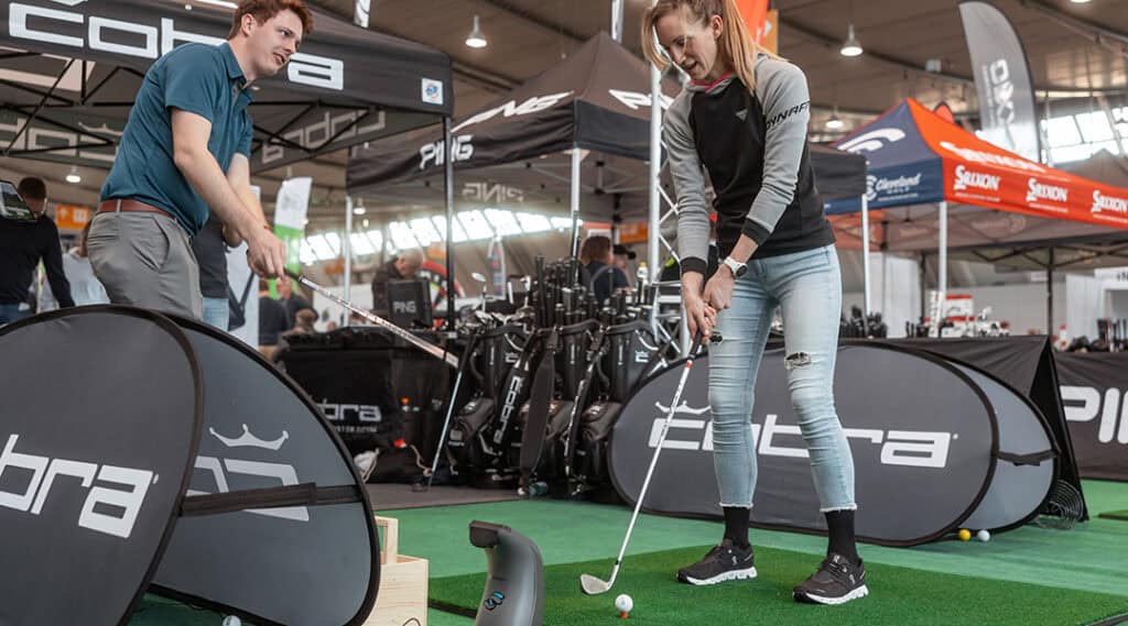 Eine Golferin testet Equipment auf einem Indoor-Grün in der Messehalle