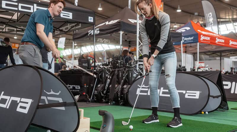 Eine Golferin testet Equipment auf einem Indoor-Grün in der Messehalle