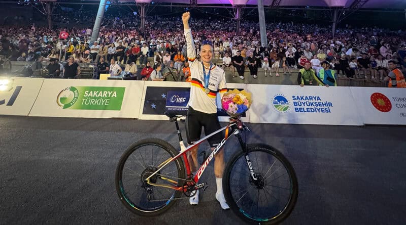 Marion Fromberger strahlt nach ihrem erfolgreichen Rennen in Sakarya und hebt die rechte Faust zum Sieg. In der linken Hand hält sie einen Blumenstrauß und ihr Corratec MTB.