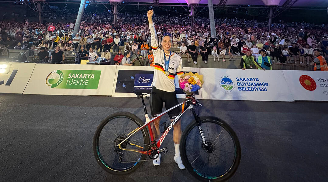Marion Fromberger strahlt nach ihrem erfolgreichen Rennen in Sakarya und hebt die rechte Faust zum Sieg. In der linken Hand hält sie einen Blumenstrauß und ihr Corratec MTB.