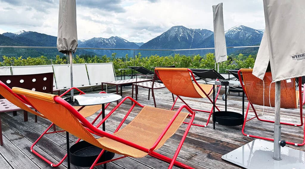 Orangefarbene Liegestühle auf der Dachterrasse des Hotel Bussi Baby vor der Tegernseer Bergkulisse.