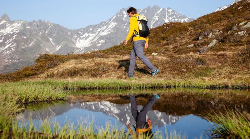 Bergwanderführer Georg Pawlata unterwegs in einer alpinen Landschaft. Im Vordergrund ein See, in dem er sich spiegelt.
