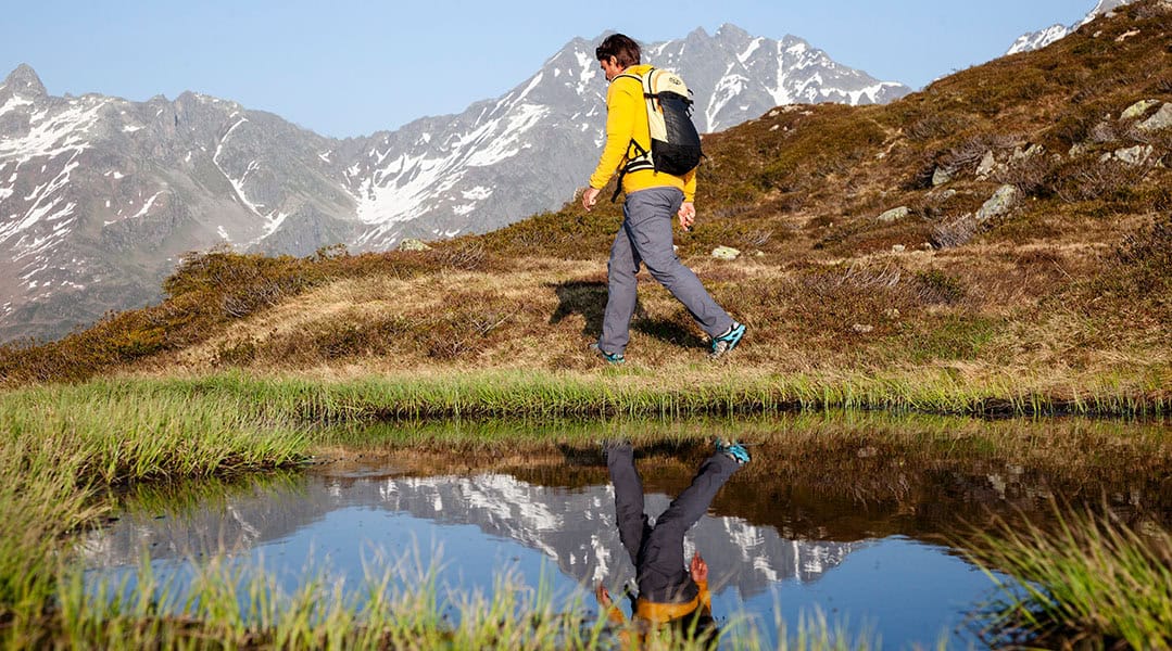 Bergwanderführer Georg Pawlata unterwegs in einer alpinen Landschaft. Im Vordergrund ein See, in dem er sich spiegelt.