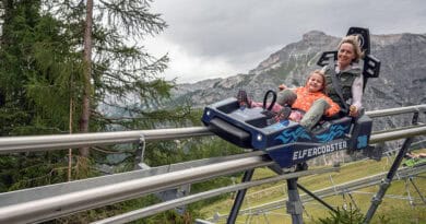 Eine Erwachsene und ein Kind fahren gemeinsam mit dem ELFERCOASTER auf einer Schienenrodelbahn vor der Bergkulisse des Stubaitals.