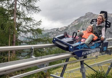Eine Erwachsene und ein Kind fahren gemeinsam mit dem ELFERCOASTER auf einer Schienenrodelbahn vor der Bergkulisse des Stubaitals.