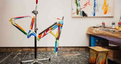 Bunt bemalter corratec LIFE S Fahrradrahmen auf einem Montageständer im Atelier.