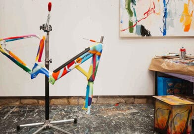 Bunt bemalter corratec LIFE S Fahrradrahmen auf einem Montageständer im Atelier.