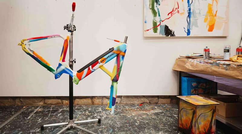 Bunt bemalter corratec LIFE S Fahrradrahmen auf einem Montageständer im Atelier.