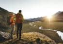Herbst im Stubaital: Zwei Wanderer blicken im goldenen Abendlicht auf eine alpine Landschaft mit Bachlauf und Stubaier Bergen.