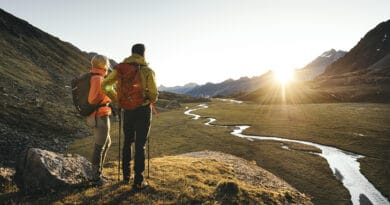 Herbst im Stubaital: Zwei Wanderer blicken im goldenen Abendlicht auf eine alpine Landschaft mit Bachlauf und Stubaier Bergen.