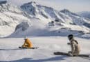 Zwei Skifahrer auf frisch präparierter Piste am Stubaier Gletscher vor verschneiter Bergkulisse.