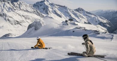 Zwei Skifahrer auf frisch präparierter Piste am Stubaier Gletscher vor verschneiter Bergkulisse.