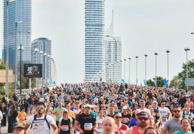 Großes Läuferfeld beim Vienna City Marathon auf einer breiten Straße, im Hintergrund die moderne Skyline von Wien.