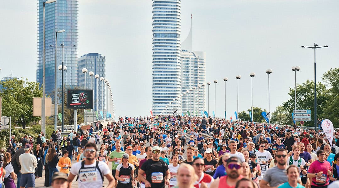 Großes Läuferfeld beim Vienna City Marathon auf einer breiten Straße, im Hintergrund die moderne Skyline von Wien.