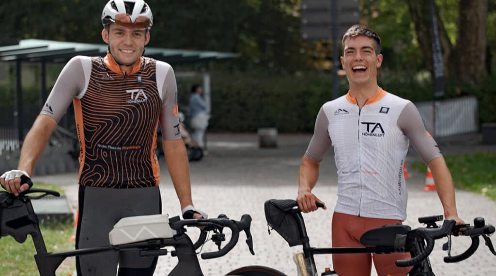 Zwei Rennradfahrer stehen nach dem Race Across Austria lächelnd mit ihren Fahrrädern am Zielort Feldkirch.