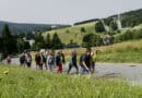 Wandergruppe bei Oberwiesenthal im Erzgebirge mit Skisprungschanzen und bewaldeten Bergen im Hintergrund.