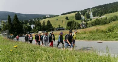 Wandergruppe bei Oberwiesenthal im Erzgebirge mit Skisprungschanzen und bewaldeten Bergen im Hintergrund.
