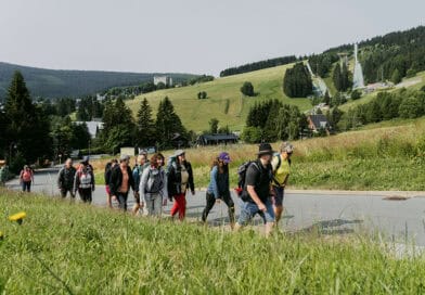 Wandergruppe bei Oberwiesenthal im Erzgebirge mit Skisprungschanzen und bewaldeten Bergen im Hintergrund.