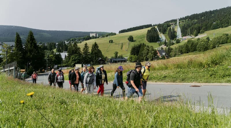 Wandergruppe bei Oberwiesenthal im Erzgebirge mit Skisprungschanzen und bewaldeten Bergen im Hintergrund.